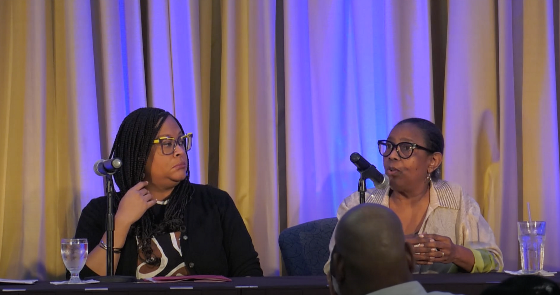 Two women are sitting at a table talking into microphones.