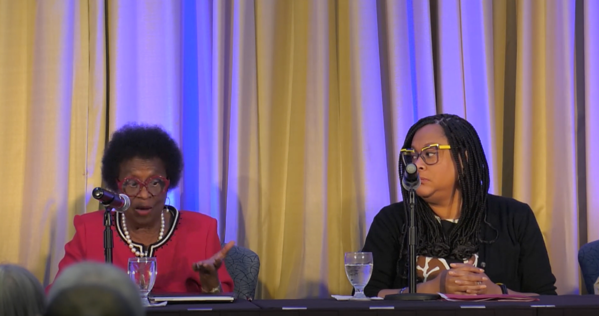 Two women are sitting at a table talking into microphones.