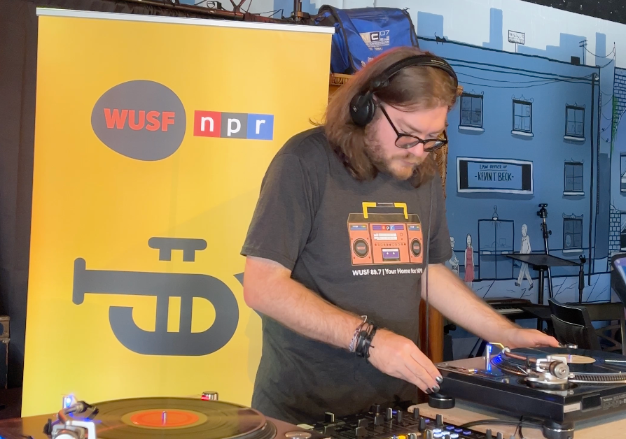 A man wearing headphones is playing a record in front of a wusp npr sign