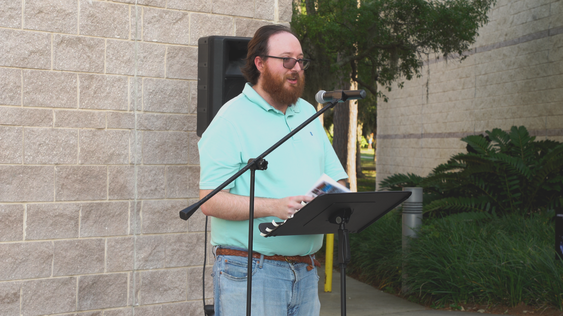 A man with a beard is standing in front of a microphone holding a book