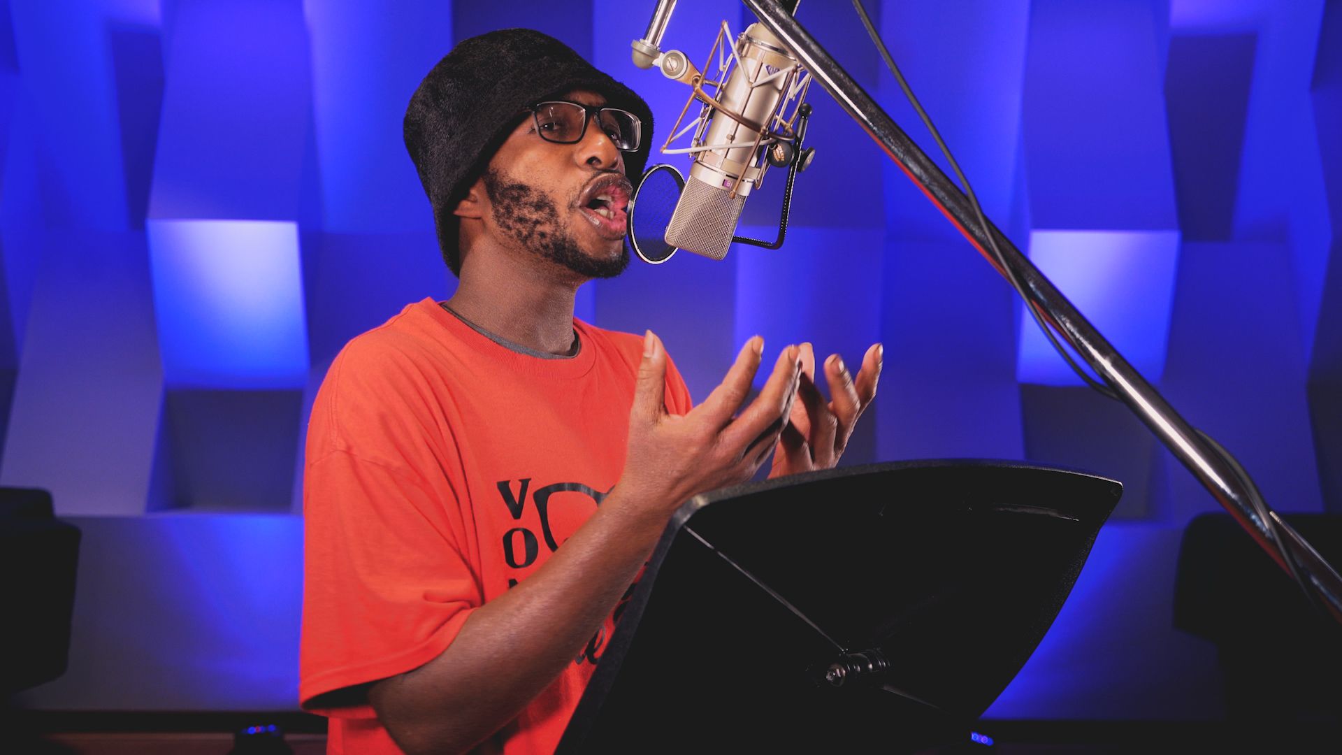 a man in an orange shirt is singing into a microphone