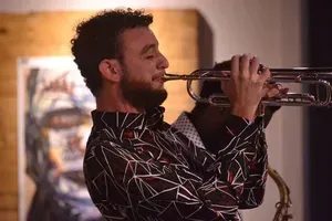 A man is playing a trumpet in front of a painting.