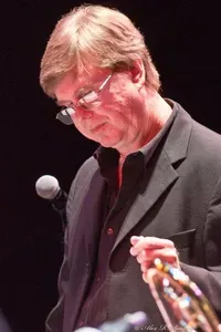 A man in a suit and glasses is playing a trumpet on a stage.