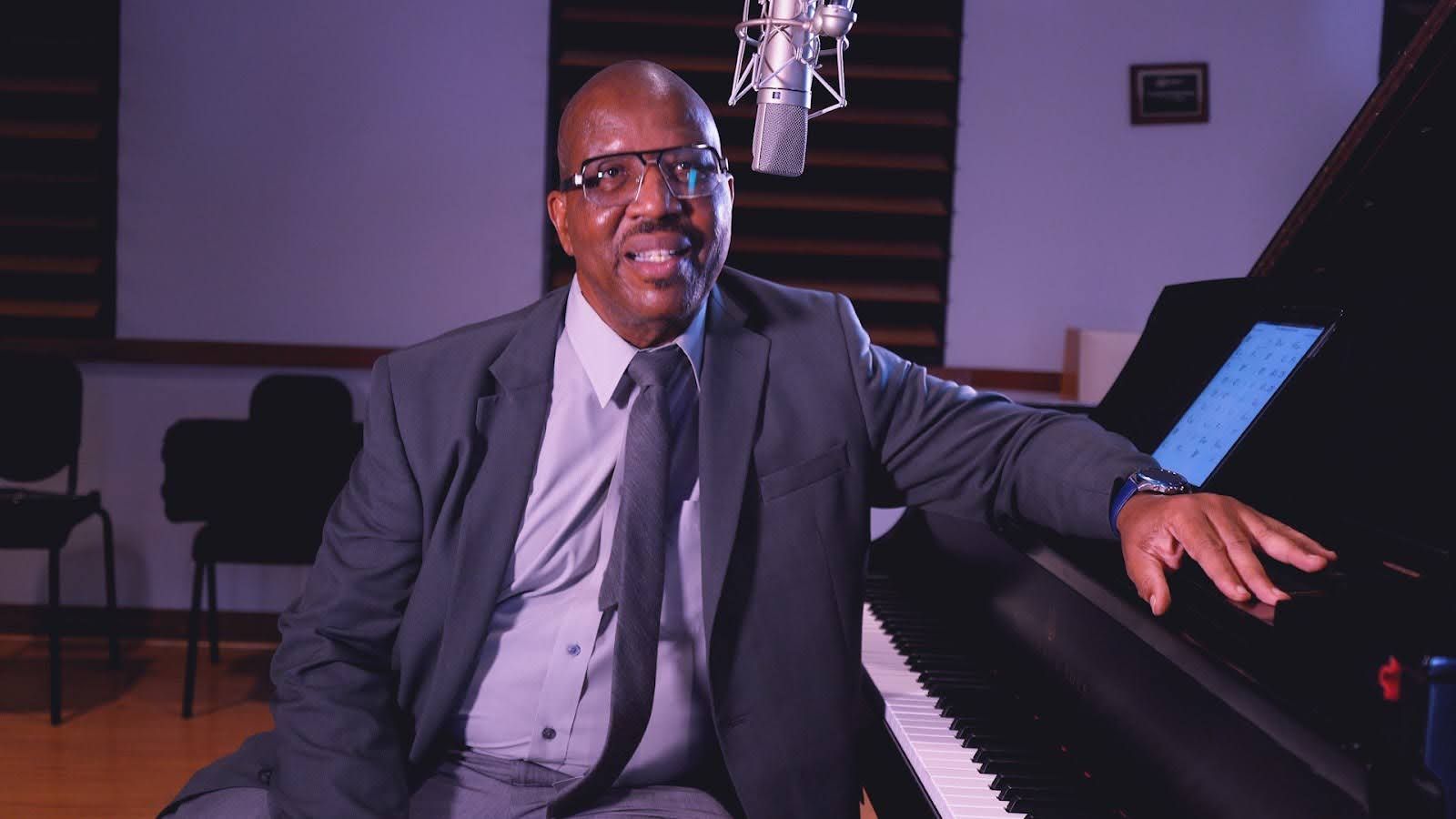 A man in a suit and tie is sitting at a piano in front of a microphone.