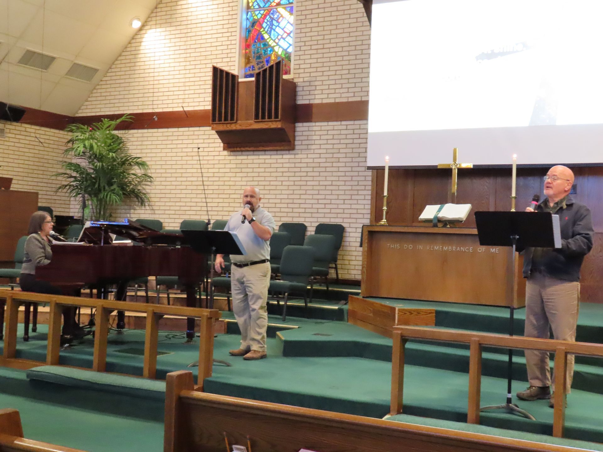 Two men singing in a church with a woman playing a piano
