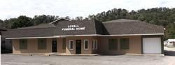 Low brick and tan community center with a sign above the entrance, set against wooded hills