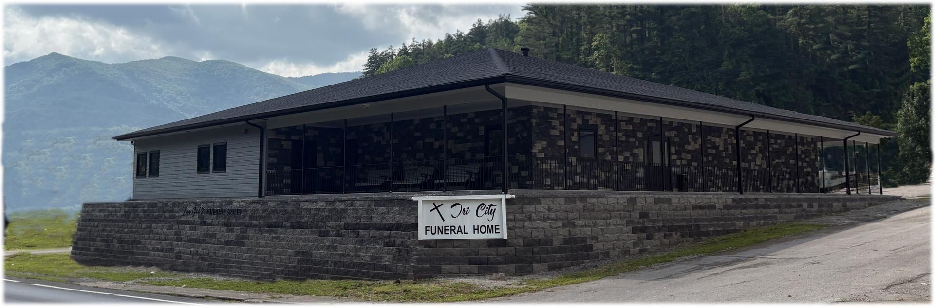 Stone building with a dark roof in a rural mountain setting, with a sign on the front wall.