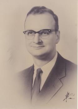 Studio portrait of a man in a suit and glasses, posed against a plain background.