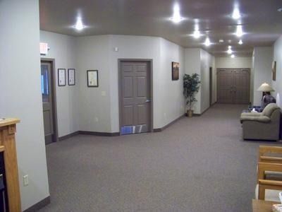 Empty hallway with beige walls, brown carpet, closed doors, recessed lights, and a couch along the right wall
