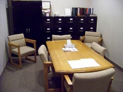 Conference room with wooden table, beige chairs, black cabinets, and papers on the table.