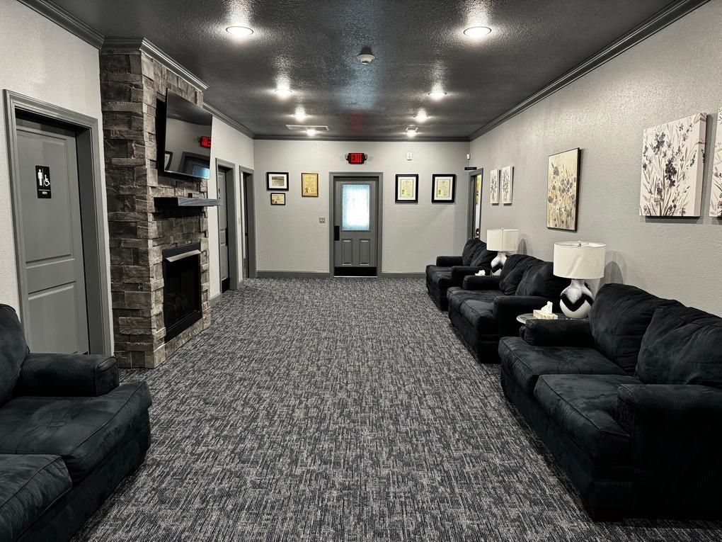 Long lounge with black sofas, patterned carpet, white walls, and framed art under recessed ceiling lights