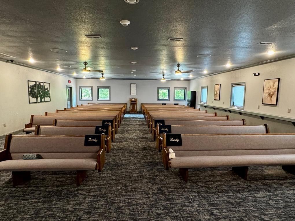 Empty church sanctuary with rows of pews facing a central aisle and stained-glass windows.