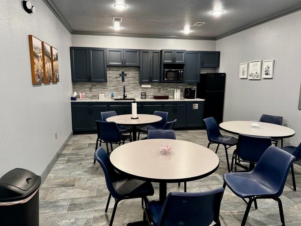 Small kitchenette with tables and blue chairs in a waiting or break room.