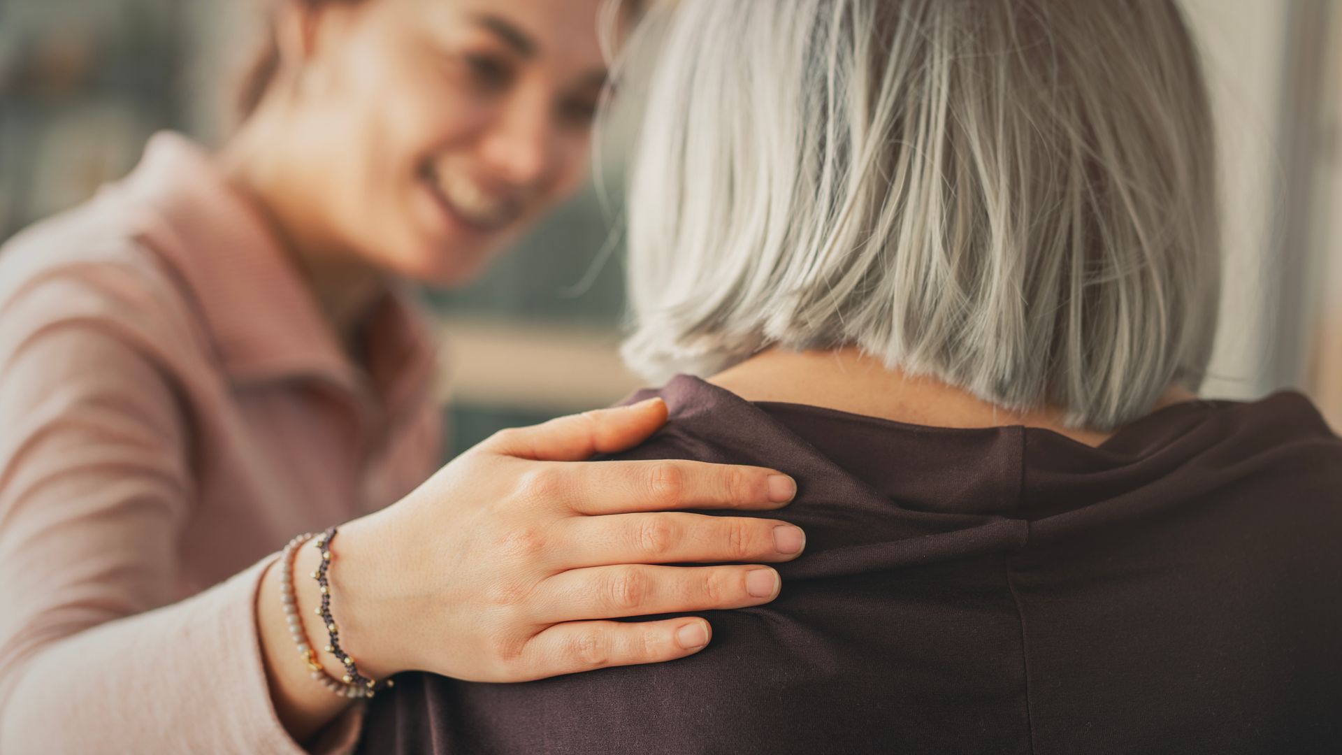 Woman gently comforts another person with a hand on their shoulder indoors.