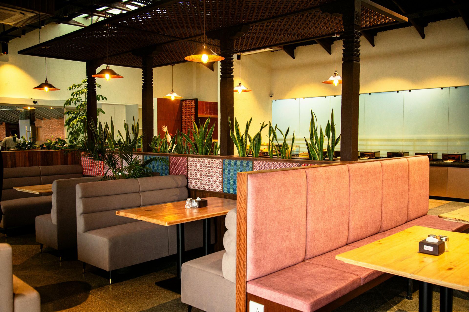 Modern restaurant interior with pink and gray booths, wooden tables, hanging lights, and potted plants