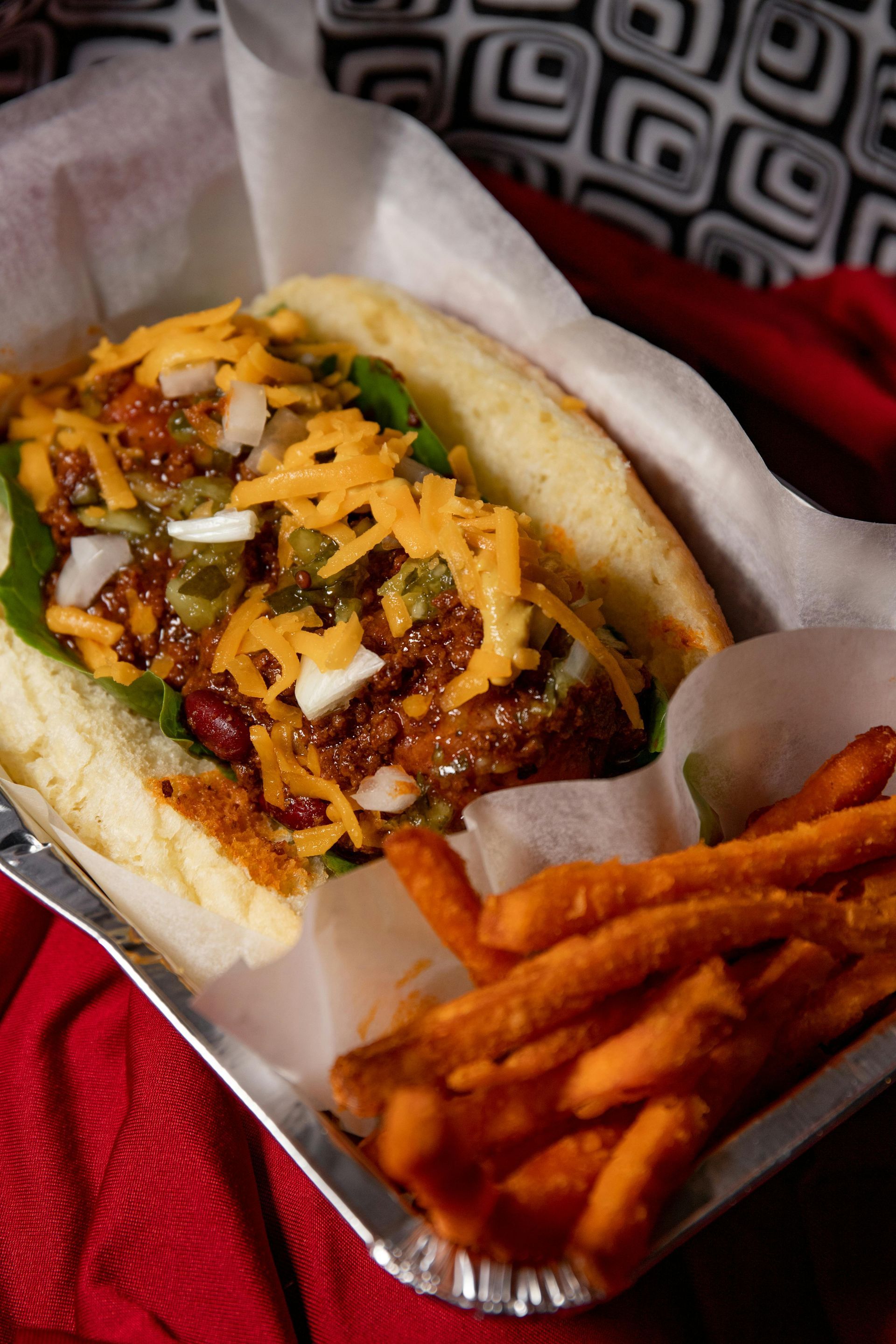Loaded sandwich with cheese and slaw, served with sweet potato fries in a foil tray