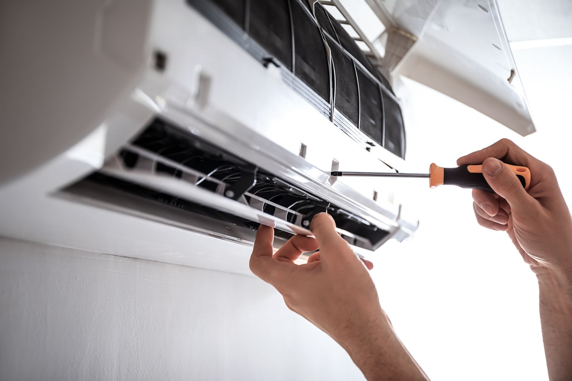 Personne réparant un climatiseur avec un tournevis.