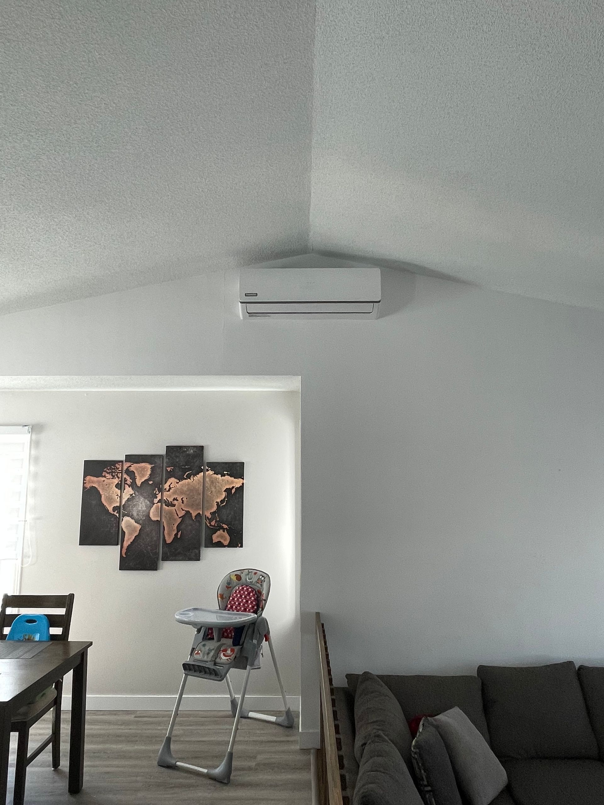 Climatiseur fixé sur un mur blanc dans un salon. On y voit un canapé, une table et une chaise haute.