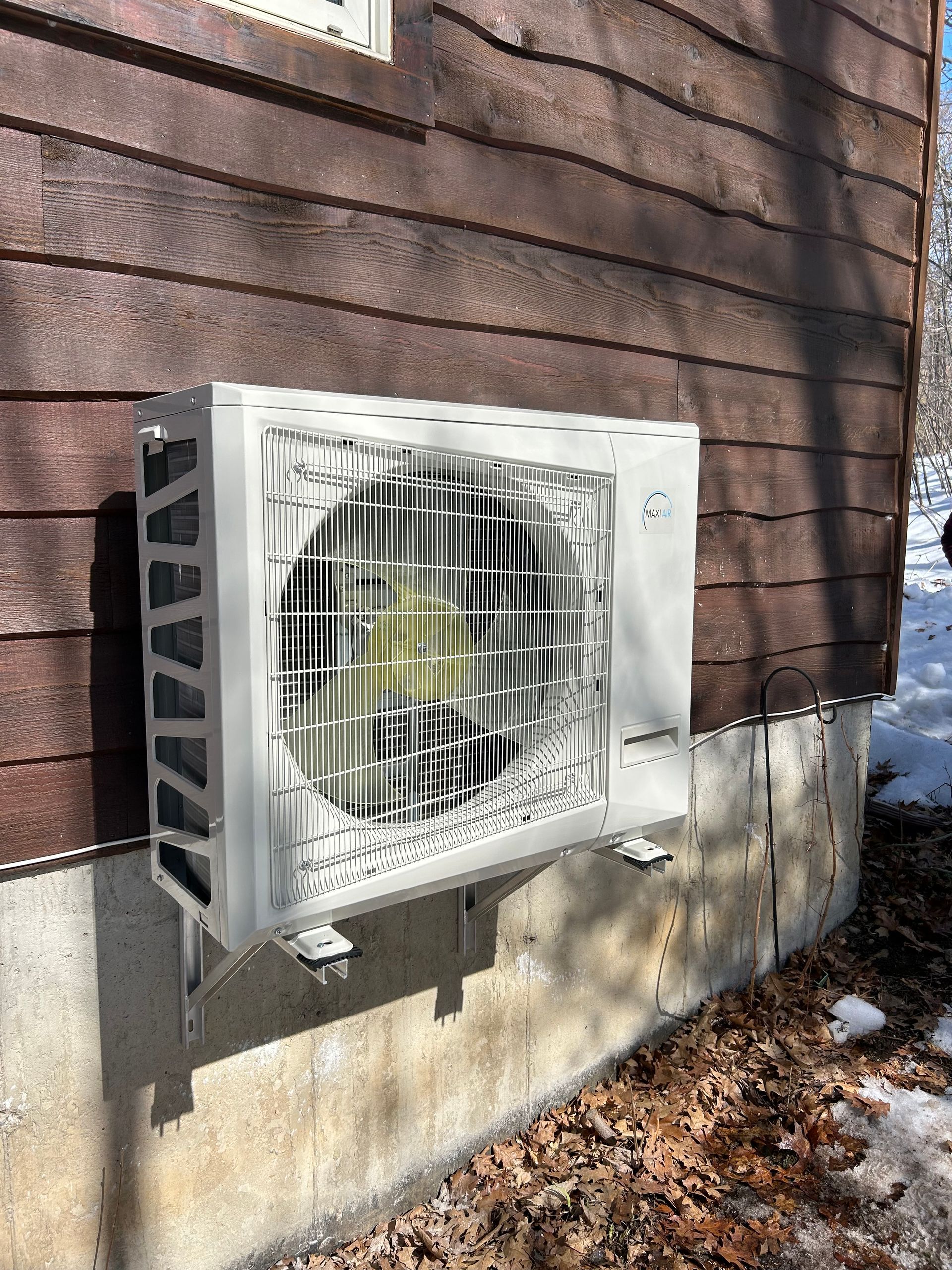 A white air conditioner is mounted on the side of a wooden house.