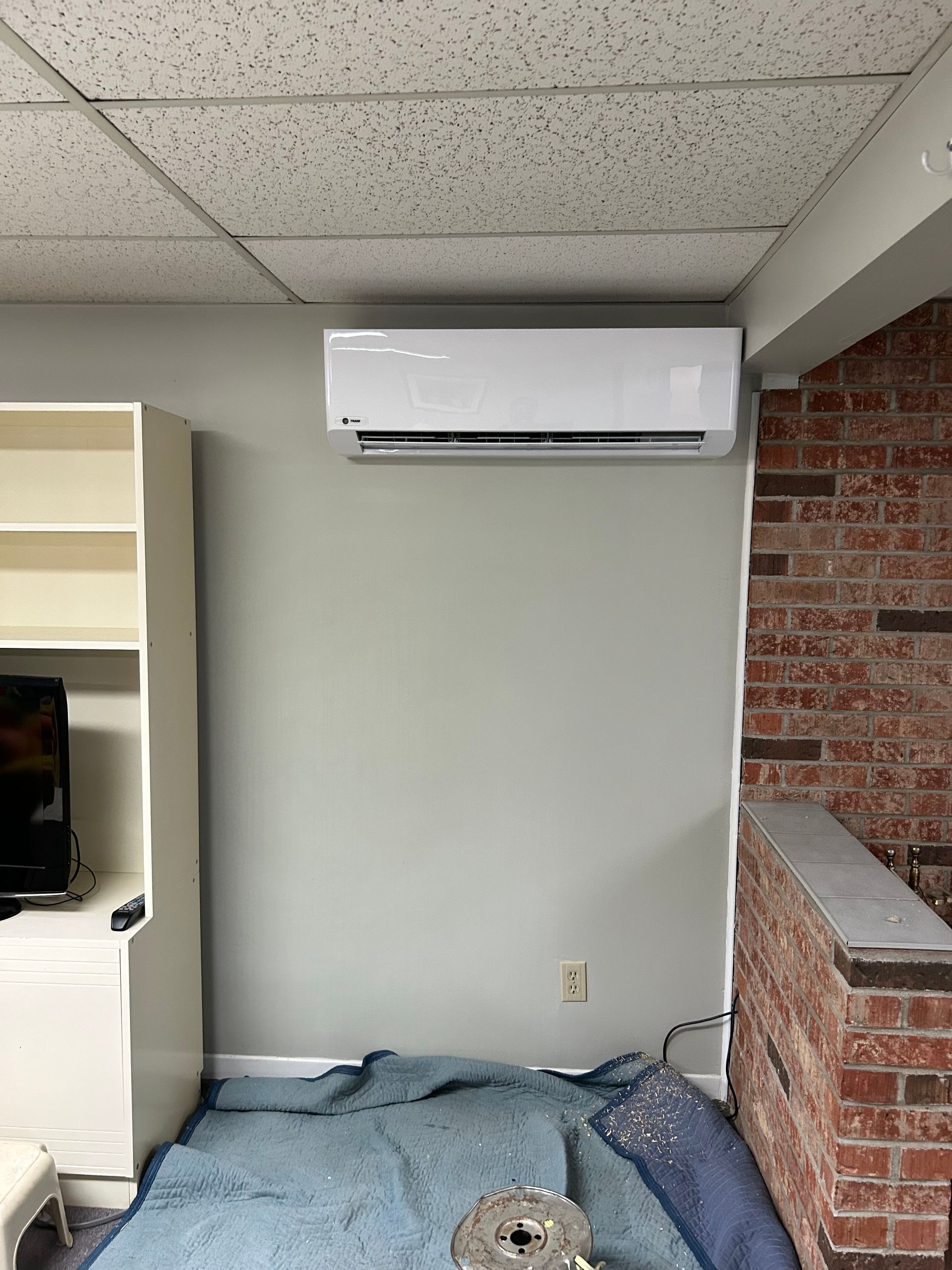 A room with a wall mounted air conditioner and a brick wall.