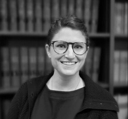 a woman wearing glasses and a black sweater is smiling in a black and white photo .