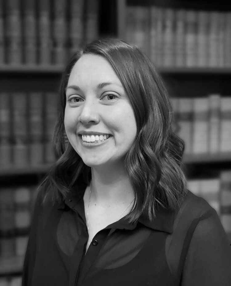 A black and white photo of a woman smiling in front of a bookshelf.
