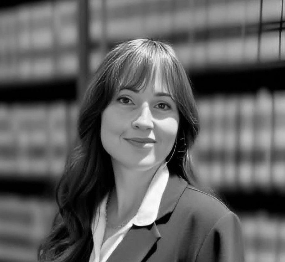 A black and white photo of a woman smiling in front of a bookshelf.