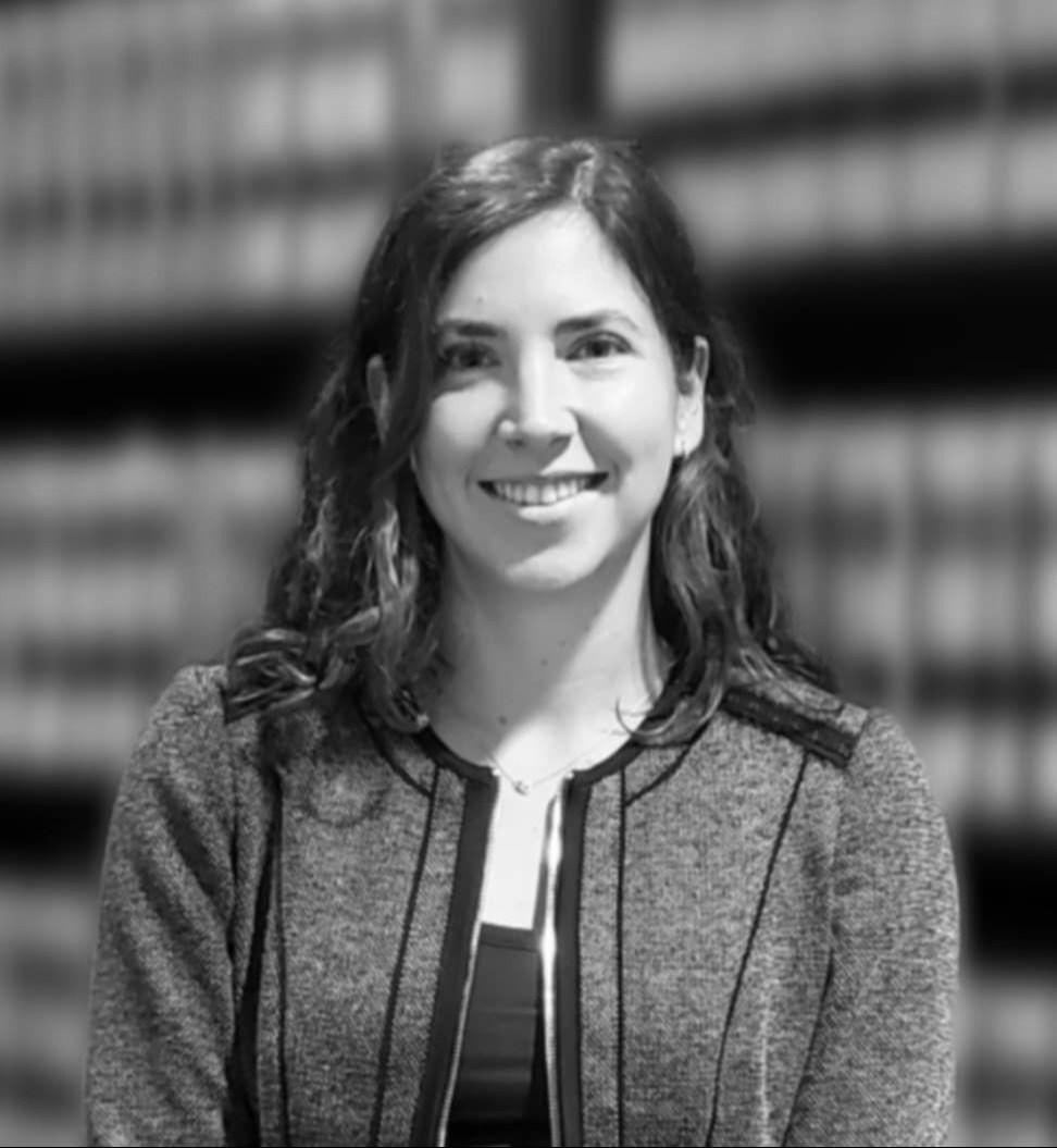 A black and white photo of a woman smiling in front of a bookshelf.
