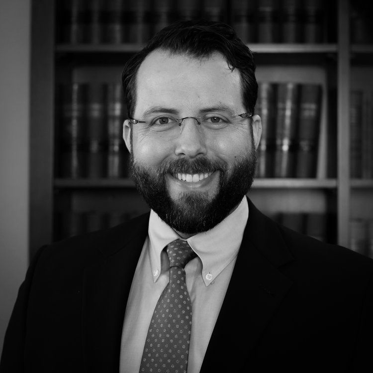 a man with glasses and a beard is smiling in front of a bookshelf
