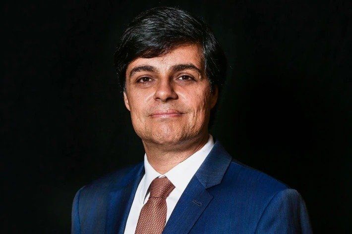 Um homem de terno e gravata está em frente a um fundo preto.