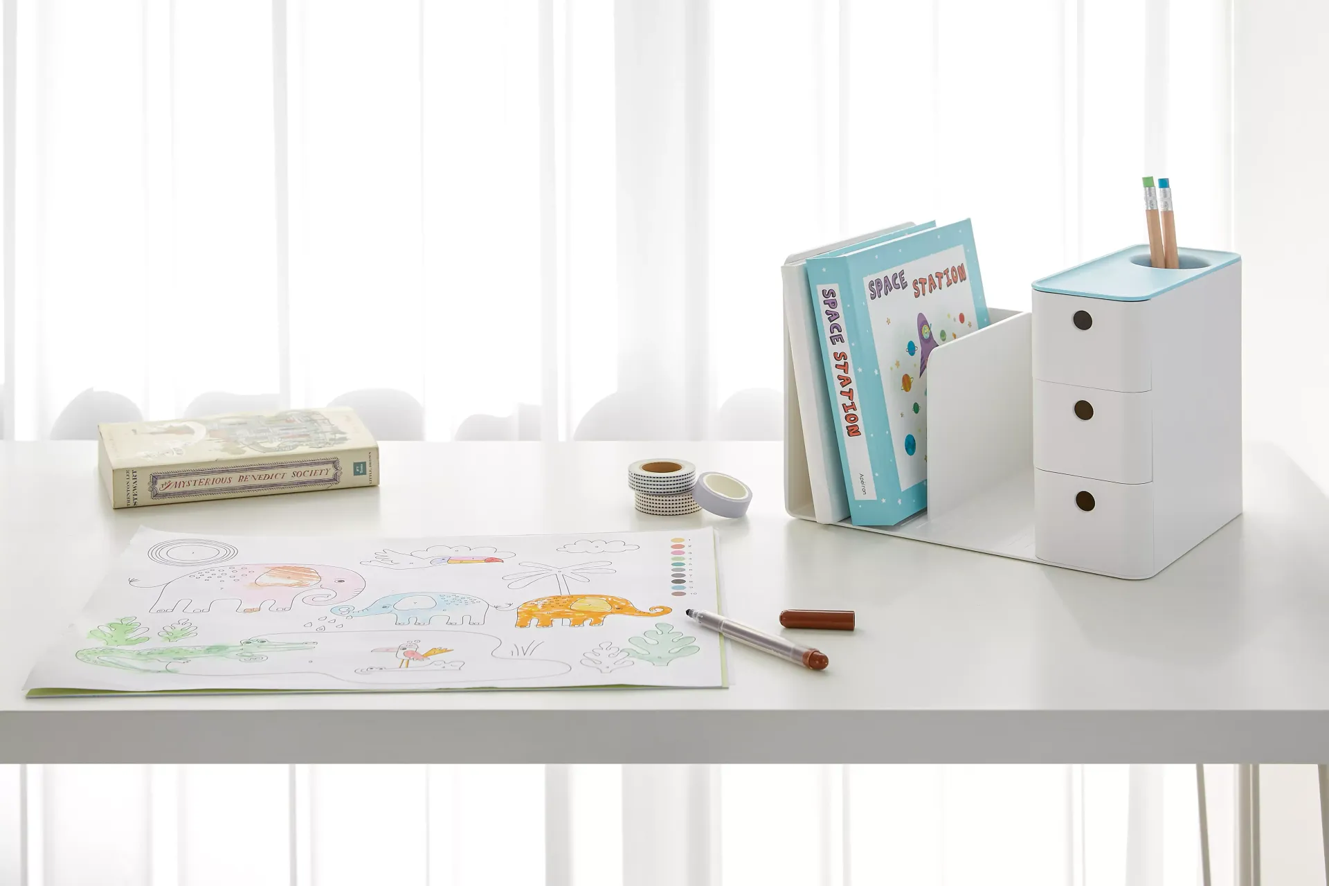 Una mesa blanca con un dibujo y libros sobre ella en un organizador de litem.