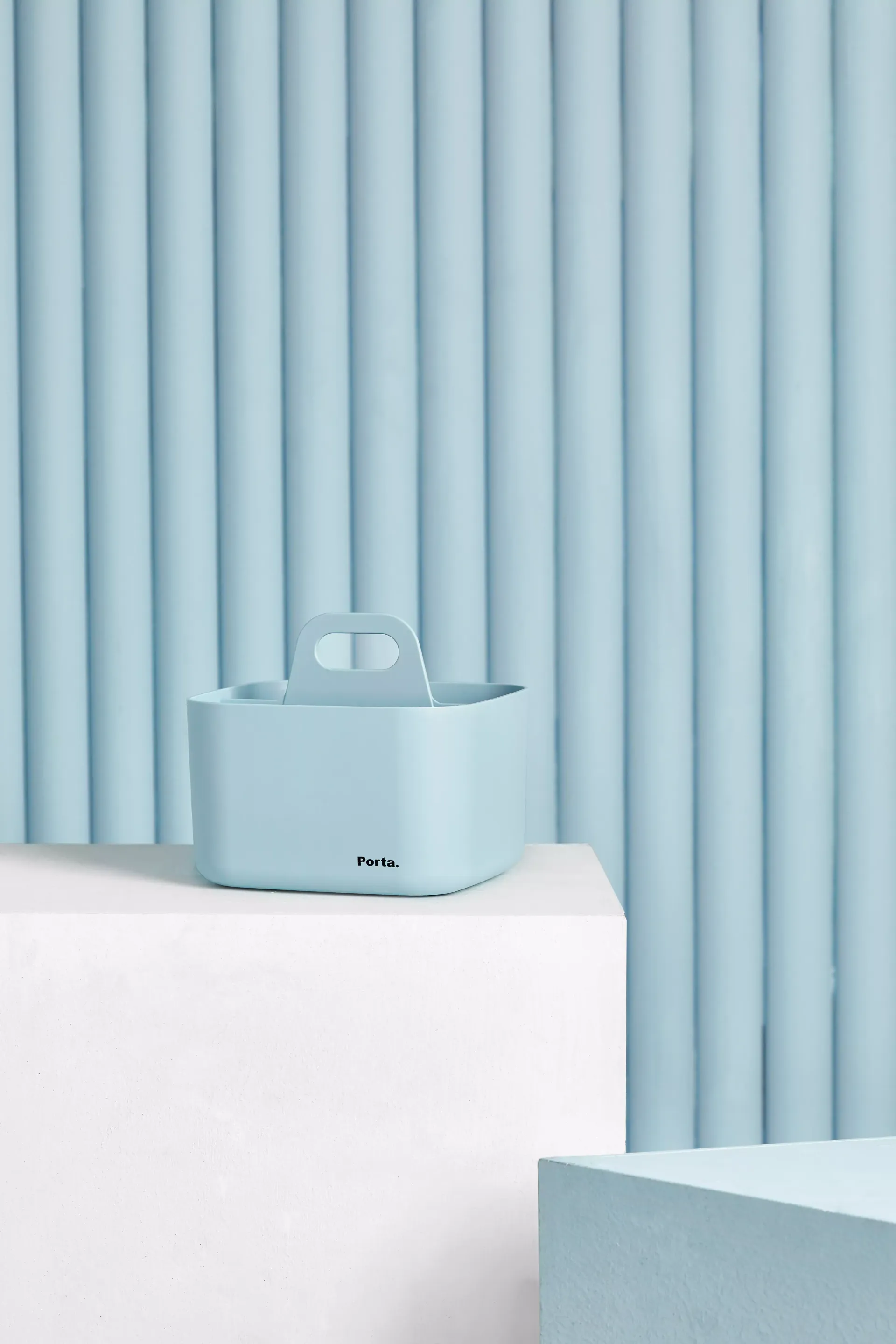 Un recipiente azul con asa está sobre un cubo blanco frente a una pared azul.