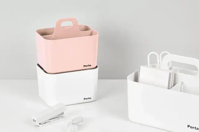 Un recipiente rosa y blanco con asa está sobre una mesa junto a una grapadora y unas tijeras.