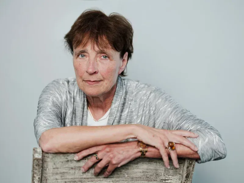 Een vrouw leunt op een houten stoel met haar handen op haar schouders.