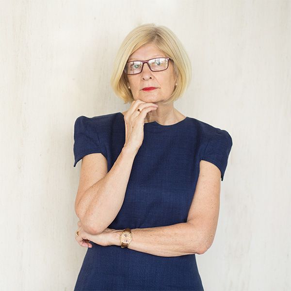 Een vrouw met een bril en een blauwe jurk heeft haar hand op haar kin