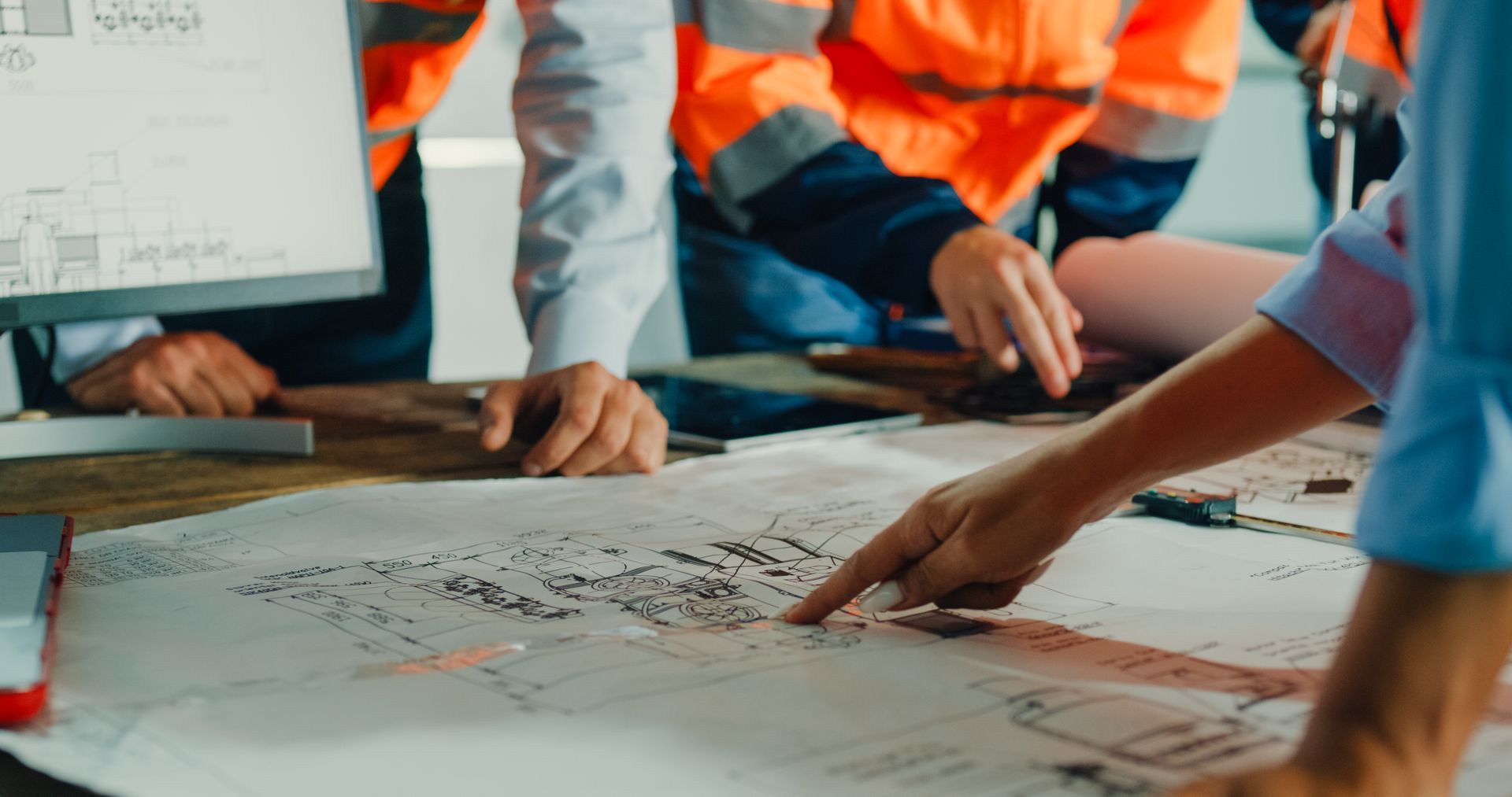 Engineers in safety vests reviewing blueprints on a table.