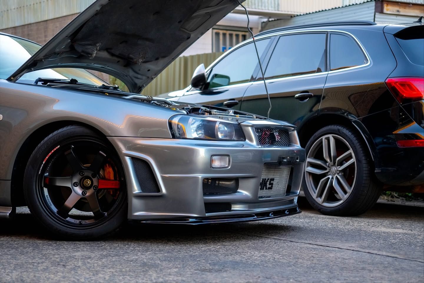 Silver sports sedan with hood open parked beside a black SUV on a street