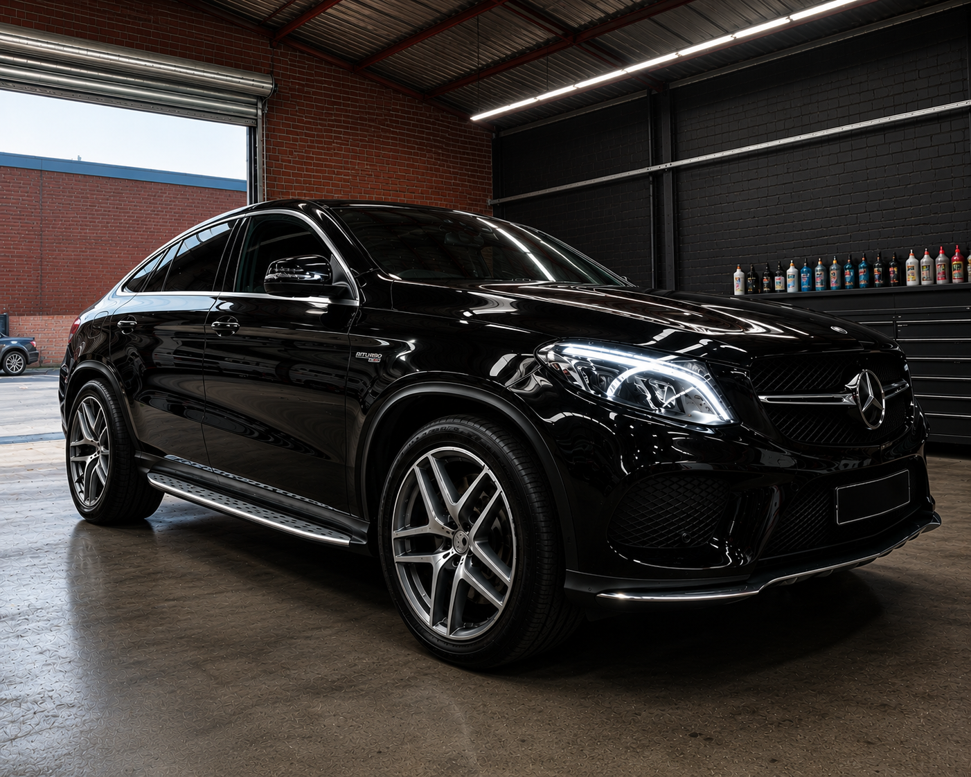 Black Mercedes SUV parked indoors in a garage or showroom, side view with glossy reflections.