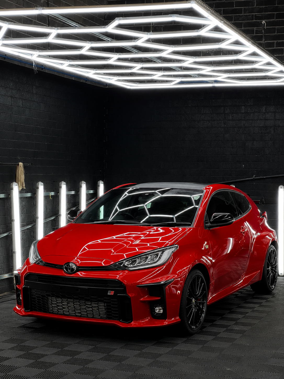 Red sports hatchback in a dark studio with bright geometric ceiling lights