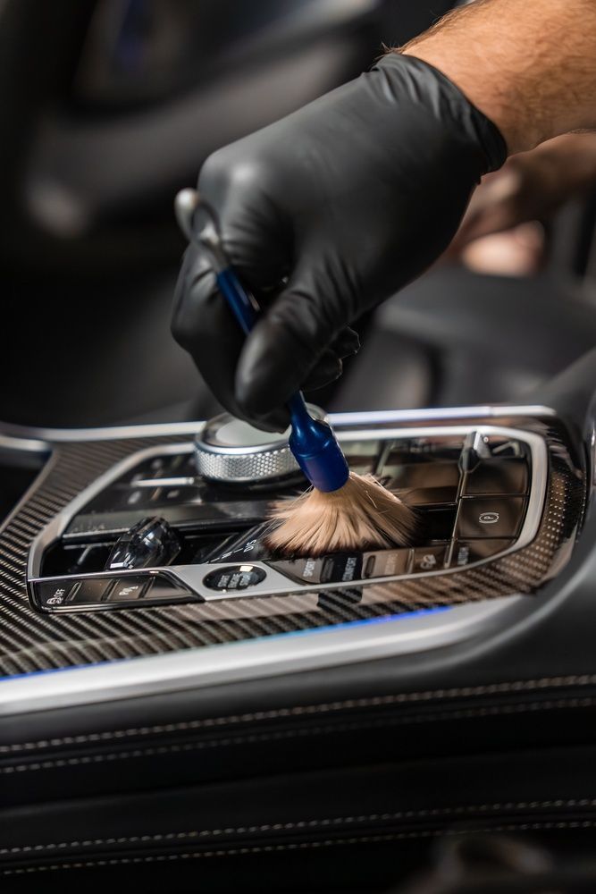 Gloved hand cleaning a car’s center console with a brush and detailing tool