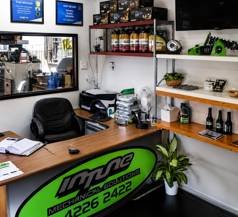 Small auto shop office with wooden counter, shelves of products, black chair, and green logo sign.