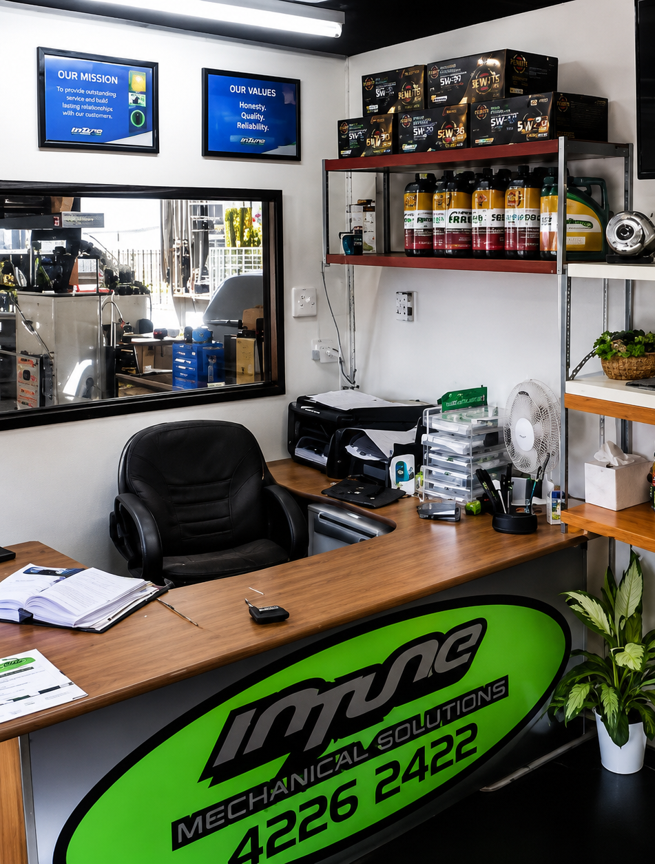 Auto repair shop reception desk with black chair, shelves of oil bottles, and green branded counter sign