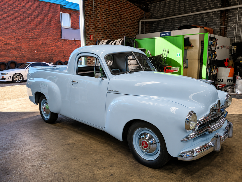 White vintage pickup truck parked indoors near brick walls and green equipment