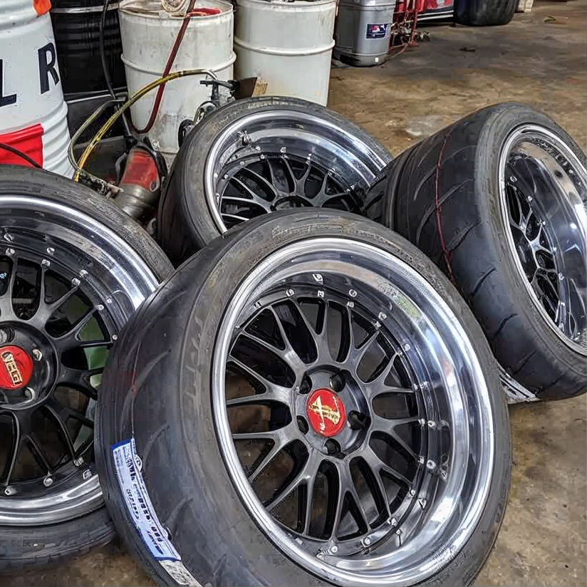 Stacked black alloy wheels with red center caps in a workshop.