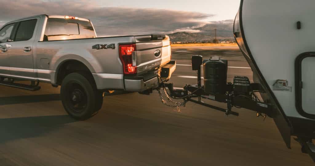 A silver truck is towing a trailer down a road.