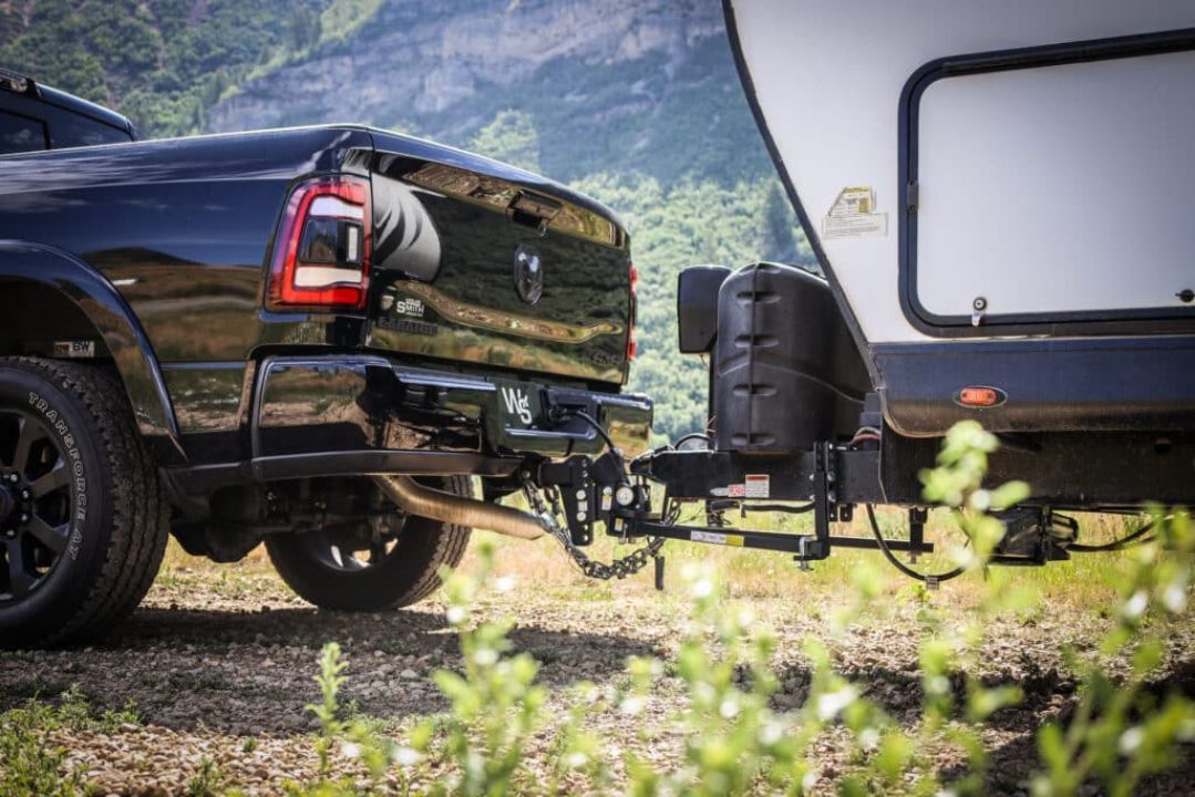 A black truck is towing a trailer in a field.