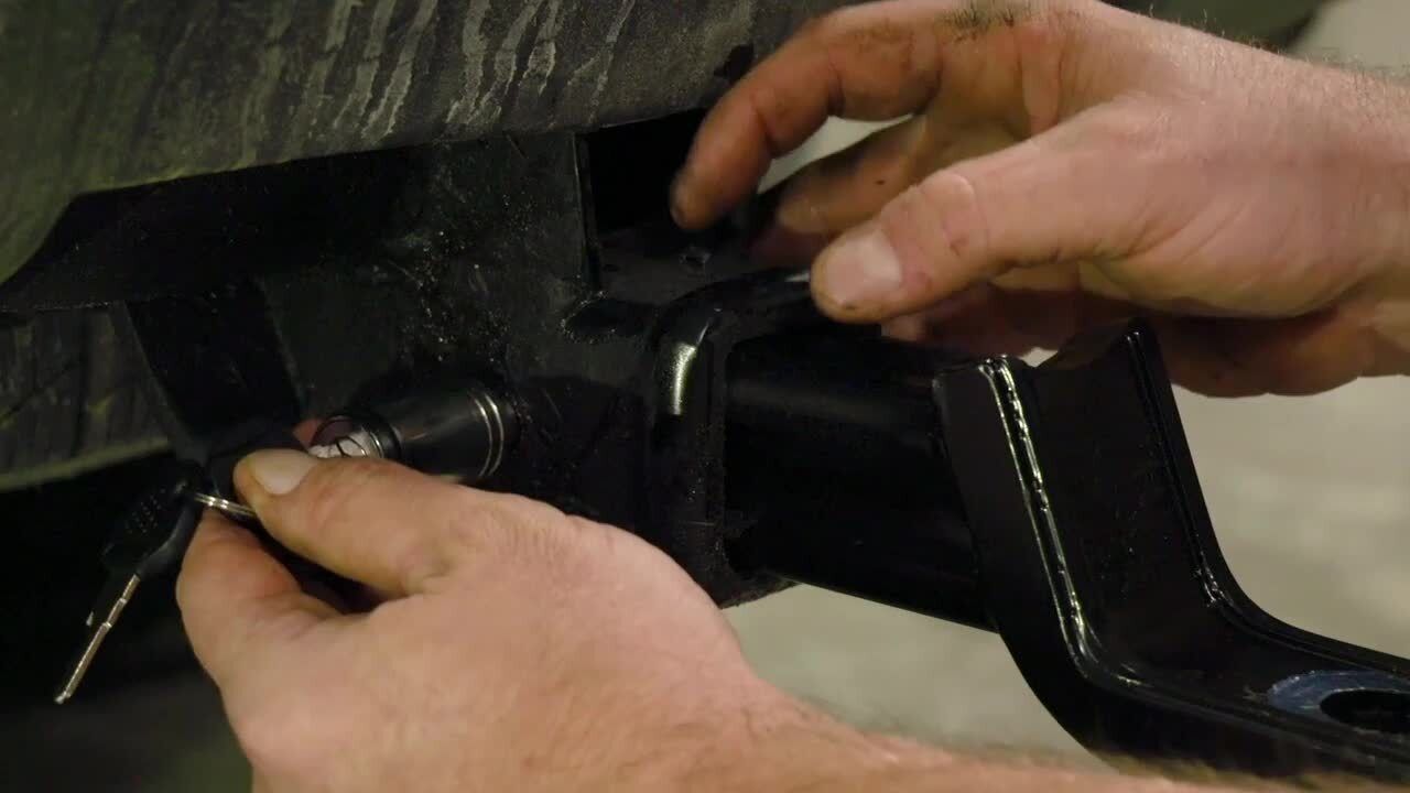 A person is fixing a trailer hitch on a car.