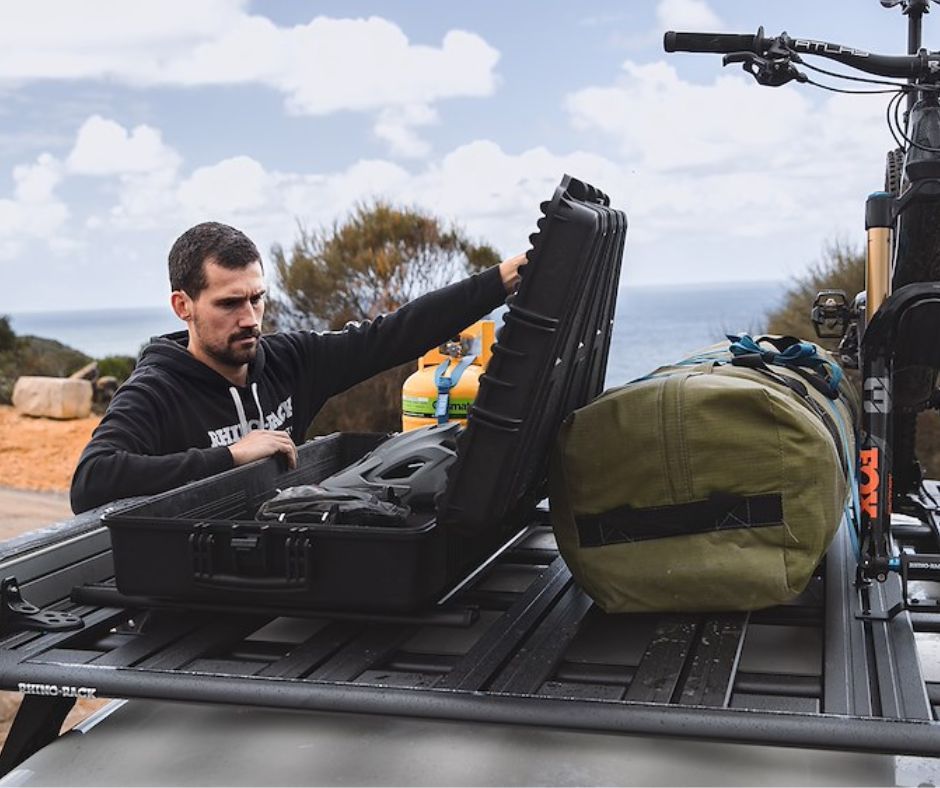 A man is putting a case on top of a roof rack.