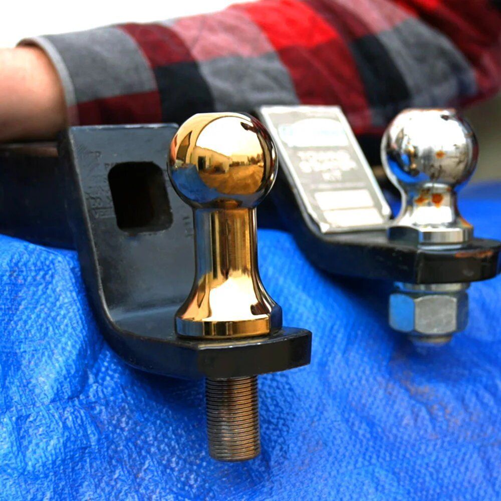 A person is laying on a blue tarp holding a pair of trailer hitch balls