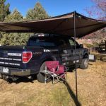 A truck is parked under a canopy at a campground.